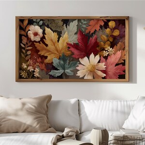 Puede incluir: Impresión botánica enmarcada con hojas y flores otoñales. La obra presenta una variedad de formas y colores de hojas, incluyendo rojo, amarillo y verde, con flores blancas y amarillas. El marco de madera añade un toque rústico.