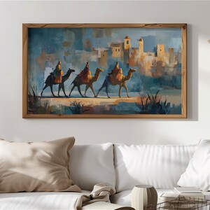 Puede incluir: Impresión artística enmarcada que representa tres camellos con jinetes en un paisaje desértico. La obra de arte utiliza una paleta de colores cálidos con azules, naranjas y marrones. El fondo muestra una ciudad con torres.