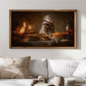 May include: A framed print showing a raccoon in a chef's hat, with pies and candles on a table. The artwork has a warm colour palette, focusing on the food and the raccoon. The scene creates a cosy, autumnal atmosphere, reminiscent of a harvest feast.