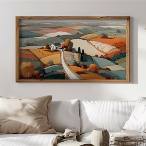 May include: A framed landscape painting shows a rural scene with fields in orange, yellow, blue, and green hues. A white house with a black roof is on a hill, and a road meanders through the fields. The artwork is displayed above a white sofa.