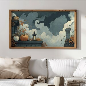 May include: A framed art print depicting a fall scene with pumpkins, a lantern, and a chimney against a cloudy sky. The artwork features a wooden frame and is displayed above a white sofa, creating a cozy, autumnal atmosphere.