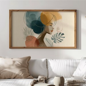Könnte beinhalten: Aquarelldruck in einem Holzrahmen. Das Kunstwerk zeigt das Profil einer Frau mit geschlossenen Augen und roten Lippen. Abstrakte Formen in Türkis, Orange und Gelb umgeben ihren Kopf. Tropische Blätter sind ebenfalls im Design enthalten.