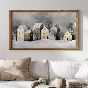 Può includere: Un'opera d'arte murale rettangolare in una cornice di legno che raffigura un paesaggio invernale con diverse case immerse nella neve. Le case sono dipinte in tonalità di bianco e grigio con finestre gialle luminose e alberi spogli.