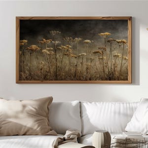 Puede incluir: Impresión enmarcada que presenta un campo de flores secas en tonos beige y marrón. La obra de arte tiene una estética vintage, con un fondo oscuro y brumoso. El marco de madera añade un toque rústico, para la decoración del hogar.