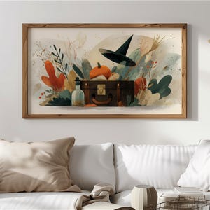 Op de afbeelding: Waterverfschilderij van een Halloween-tafereel. Een zwarte heksenhoed zweeft boven een vintage koffer, met een pompoen en een fles. Het kunstwerk toont herfstbladeren in tinten oranje, groen en beige, geplaatst in een houten frame.