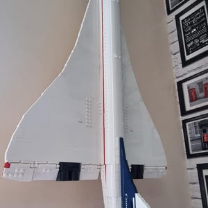 May include: A white model of a Concorde supersonic jet airplane, with red and blue accents. The model is mounted on a wall, showcasing its wingspan and streamlined design. The tail features the word "Concorde".