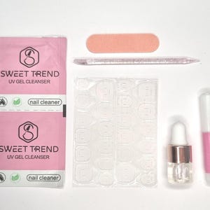 Könnte beinhalten: Ein Nagelset mit verschiedenen Artikeln, darunter zwei rosa-weiße Päckchen mit der Aufschrift "SWEET TREND UV GEL CLEANSER", eine pfirsichfarbene Nagelfeile, ein klarer Nagelhautschieber, ein Bogen mit transparenten Nagelaufklebern, eine kleine Flasche mit einer Pipette und ein rosa-weißer Nagelkleberstift.