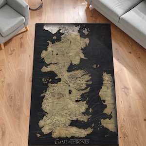 May include: A rectangular rug featuring a map of a fictional land, with a black background and a gold-colored map design. The words "GAME OF THRONES" are printed in gold at the bottom. The rug is placed on a wooden floor.