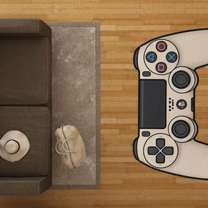 Peut inclure: Un tapis beige et noir en forme de manette de jeu sur un sol en bois. Le tapis représente une manette de jeu vidéo, avec des boutons colorés et des pavés directionnels. Un canapé marron, un chapeau et un sac sont également visibles.