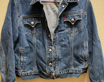 May include: A blue denim jacket with a button closure and two front pockets. The jacket has a Levi's label on the left pocket.