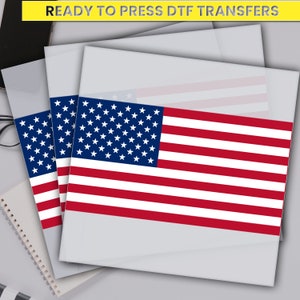 May include: Three sheets of clear transfer paper with an American flag design printed on them. The sheets are stacked on top of each other. The text "READY TO PRESS DTF TRANSFERS" is printed in yellow on a black background at the top of the image.