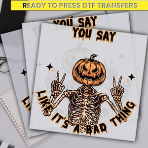 May include: DTF transfers featuring a Halloween design. The design includes a skeleton with a jack-o'-lantern head, making a peace sign with its hands. The text reads "YOU SAY LIKE IT'S A BAD THING."