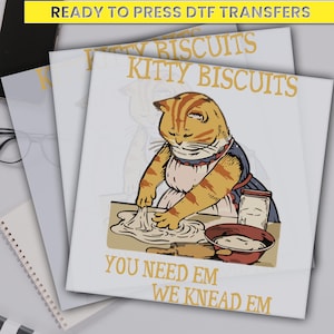 May include: A white background with a cartoon image of a cat kneading dough. The text "Kitty Biscuits" is above the cat and the text "You Need Em We Knead Em" is below the cat.