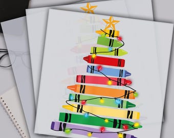May include: A stack of white DTF transfer sheets with a colorful crayon Christmas tree design. The tree is made of crayons in various colors, strung with lights, and topped with a gold star. The text "READY TO PRESS DTF TRANSFERS" is at the top.