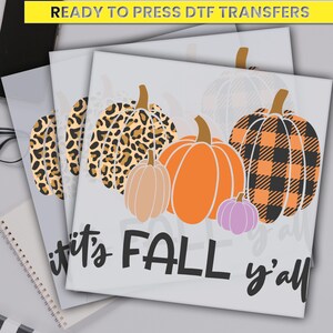 May include: Ready to press DTF transfers featuring a variety of pumpkins. The designs include leopard print, orange, and plaid patterns. The phrase "it's FALL y'all" is written in black script. A yellow banner at the top reads "READY TO PRESS DTF TRANSFERS".