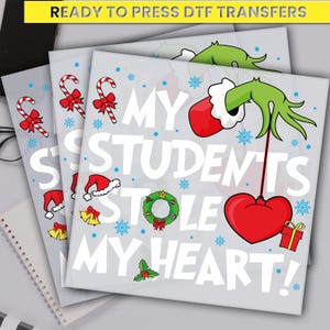 May include: DTF transfers with a Christmas theme. The design features the text "MY STUDENTS STOLE MY HEART!" with candy canes, snowflakes, Santa hats, bells, a wreath, a Grinch hand holding a heart, and a gift box.