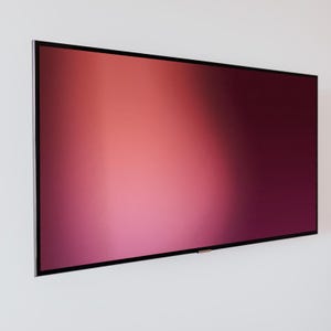 May include: A large, rectangular television with a black frame is mounted on a white wall. The screen displays a gradient of colors, transitioning from a light pink at the bottom to a deep burgundy at the top.