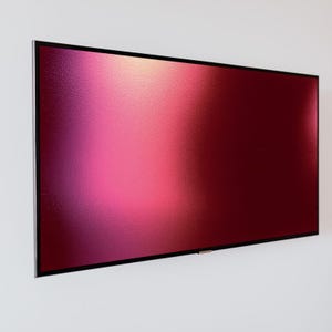 May include: A large, rectangular display with a gradient of colors from pink to deep red. The screen has a textured surface and is framed by a thin, black border with a silver edge. The display is mounted on a white wall.
