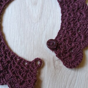Pu&ograve; includere: Un colletto in crochet color marrone rossiccio con un bordo a scalare e un bottone marrone scuro.