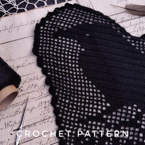 Op de afbeelding: Een close-up van een zwart haakpatroon met een geschulpte rand. Het patroon is open en luchtig, met een rasterachtig ontwerp. De woorden "CROCHET PATTERN" zijn zichtbaar onderaan de afbeelding. De achtergrond bevat vintage papier en een spoel zwart garen.