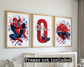 Op de afbeelding: Drie ingelijste prints met een rood en blauw superheldenpersonage met een spinnenwebontwerp. De middelste print heeft de naam "Ollie" in zwarte cursieve letters. De prints hebben een witte achtergrond met rode en blauwe verfspatten.