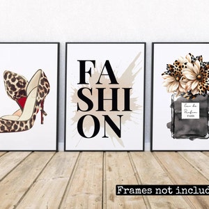 May include: Three framed prints with a fashion theme. The left print features a leopard print high heel shoe. The centre print has the word "FASHION" in black letters with a brown splatter paint background. The right print features a black and white illustration of a perfume bottle with a leopard print flower design.
