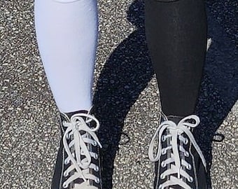 May include: A person wearing black high-top sneakers with white laces and a white sock on the left leg and a black sock on the right leg. The shoes have a white rubber sole.