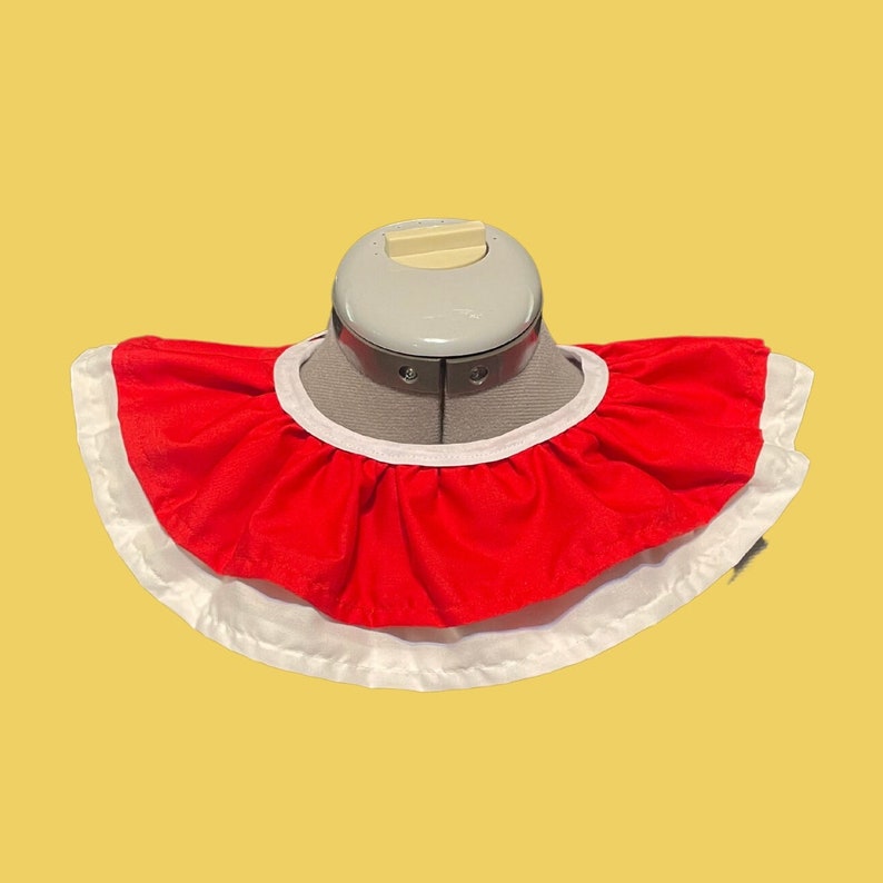 May include: A red and white ruffled collar with a white trim. The collar is made of fabric and is designed to be worn around the neck.