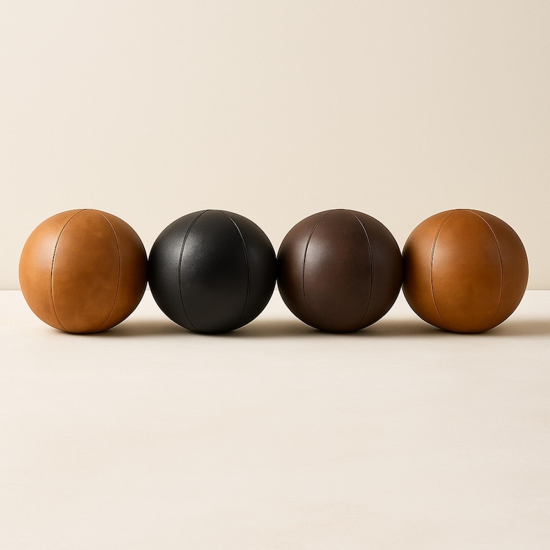 May include: Four leather decorative balls in shades of brown and black. The balls are round with vertical stitched seams. The colors include light brown, black, dark brown, and medium brown. The balls are arranged in a row.