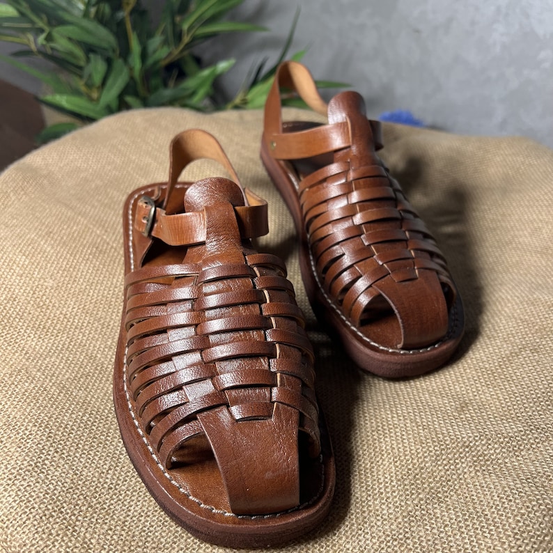 May include: A pair of brown leather sandals with a woven design. The sandals have a strap that goes around the ankle and a buckle closure.