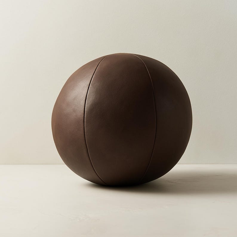 May include: A dark brown, spherical decorative object. The object has a smooth, leather-like texture and is divided into sections by vertical seams. The overall shape is round, and the color is a rich, deep brown.