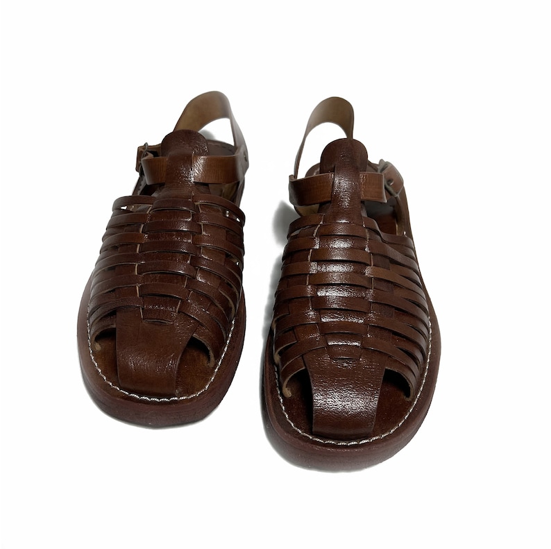 May include: A pair of brown leather sandals with a woven design. The sandals have a strap that goes around the ankle and a buckle closure.