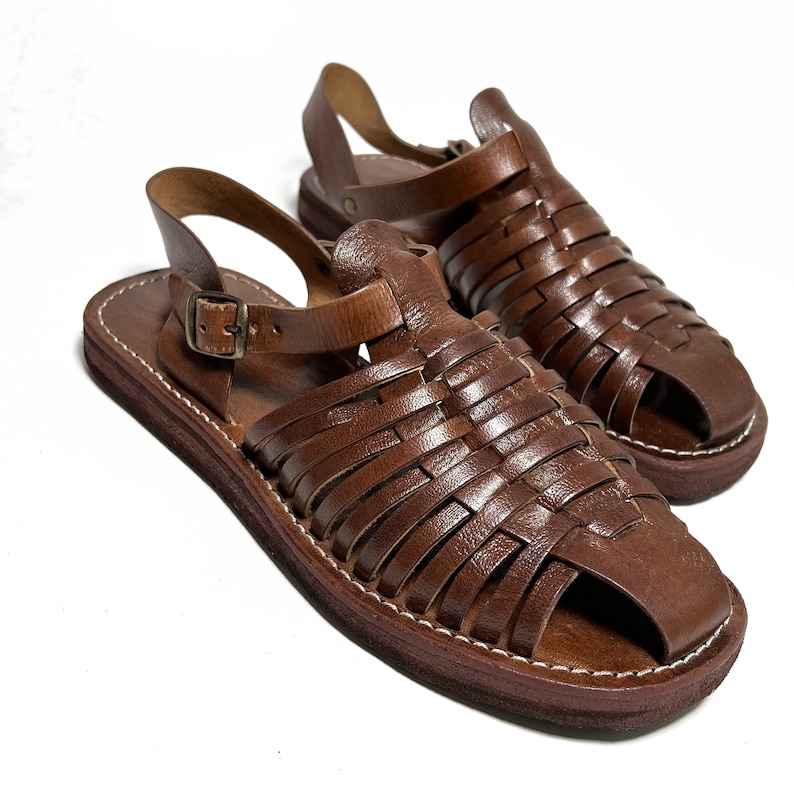 May include: A pair of brown leather sandals with a woven design. The sandals have a buckle closure and a flat sole.