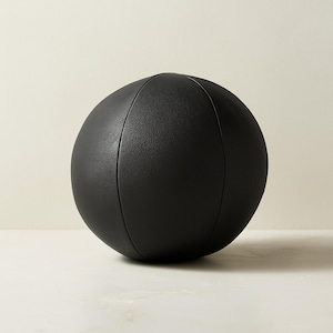 May include: A solid black, spherical decorative object with a textured surface. The ball has vertical seams and a rounded shape. The object is likely made of leather or a similar material. The background is a neutral color.