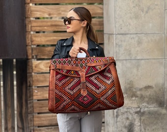 May include: A large, brown leather travel bag with a colorful woven tapestry design. The bag has a top handle and a buckle closure.