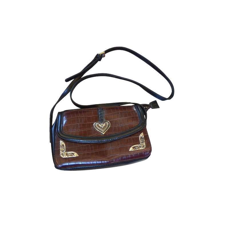 May include: Brown crossbody bag with a textured, crocodile-like pattern. The bag features a black strap and trim, with gold-colored heart and corner accents. The flap closure has a gold-colored heart-shaped embellishment.