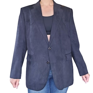 May include: A dark charcoal gray blazer with a soft, suede-like texture. The garment features a notched lapel, two front buttons, and western-style pointed yokes on the chest. It includes two flap pockets at the waist and long sleeves.