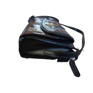May include: A brown and black handbag with a crocodile skin pattern. The bag has a black strap and a silver zipper. The flap has a silver emblem. The bag is made of leather.