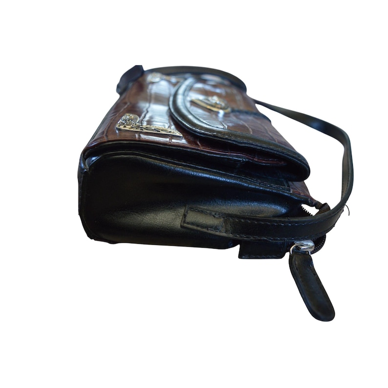 May include: A brown and black handbag with a crocodile skin pattern. The bag has a black strap and a silver zipper. The flap has a silver emblem. The bag is made of leather.