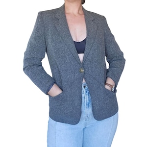 May include: A gray blazer with a single gold button closure and two front pockets. The blazer has a classic tailored design with a notched lapel and long sleeves. The blazer is made of a textured fabric.