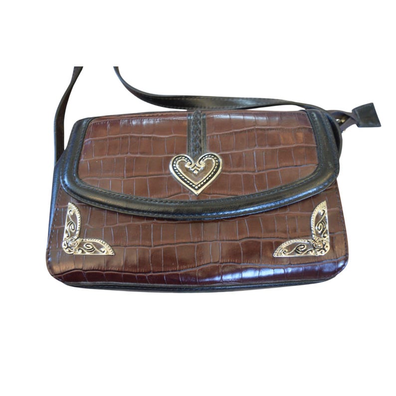 May include: Brown crossbody bag with a faux crocodile skin texture. The bag features a silver heart-shaped clasp and decorative silver corner accents. The trim is black, and the adjustable strap is also black.