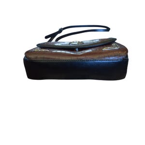 May include: A brown and black handbag with a textured, crocodile-like pattern. The bag has a black base and a flap closure with silver-colored hardware. A black strap is attached to the top of the bag.