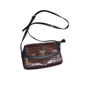 May include: Brown crossbody bag with a faux crocodile skin texture. The bag features a black strap and trim, a silver heart-shaped clasp, and decorative corner accents. The bag is designed with a flap closure.