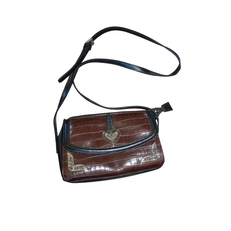 May include: Brown crossbody bag with a faux crocodile skin texture. The bag features a black strap and trim, a silver heart-shaped clasp, and decorative corner accents. The bag is designed with a flap closure.