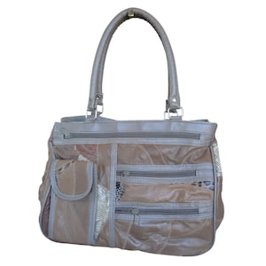 May include: A brown leather handbag with a patchwork design. The bag features multiple zippered compartments and a small pocket on the front. It has a top handle and a shoulder strap. The bag is made of various shades of brown leather.