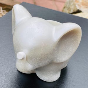 May include: A white ceramic elephant planter with a textured surface. The planter has a small hole in the top for drainage.