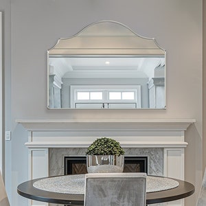 Può includere: Una sala da pranzo con un camino e uno specchio grande sopra. C'è un tavolo rotondo con quattro sedie al centro della stanza. Le sedie sono rivestite in tessuto grigio chiaro. Il camino è in marmo bianco e ha una griglia in metallo nero. Lo specchio è incorniciato da una cornice in legno bianco. Le pareti sono dipinte di grigio chiaro. Il pavimento è in legno duro.