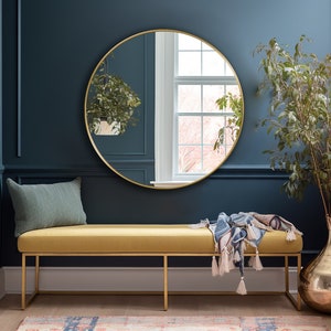 Round mirror with gold frame hung on the wall of an entryway.