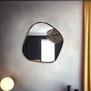 Blob shaped mirror with black frame hung on the wall of a living room.