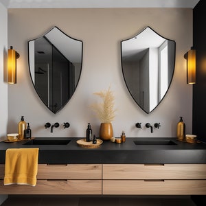 May include: A modern bathroom vanity with two sinks, black countertops, and wooden cabinets. Two black shield-shaped mirrors hang above the sinks. Each sink has a gold-colored soap dispenser and a black faucet. A vase with dried flowers sits between the sinks.